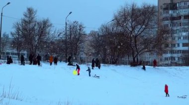 Kyiv, Ukrayna 1 Aralık 2022 Kış Tatili. Kar yağarken plastik kızaklara binen çocuklar. Kentsel alanda çocukların eğlenceli aktiviteleri.