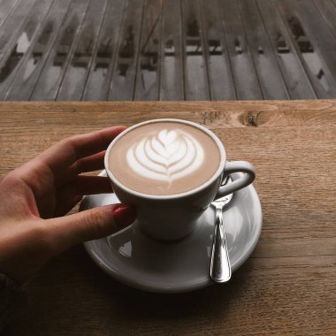 Beyaz kahve fincanı, şehir caddesinde bir kafe terasında ahşap masanın üzerinde duruyor. Yağmurlu bir günde açık havada sabah kahvesi. Kapuçino, kadın elinde latte fincanı..