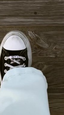 Tahta patika ve siyah beyaz spor ayakkabılı kadın bacakları yukarıdan yavaş çekim video görüntüsü. Seyahat etmek, dışarıda yürümek. Dikey seyahat videosu. 