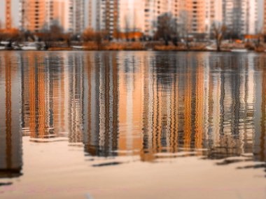 Yüksek çok katlı binaların sonbahar mevsiminde yansıdığı kentsel bir ortamda sakin su yüzeyi. Yüksek binalar. Sonbaharda şehir manzarası görünümü.