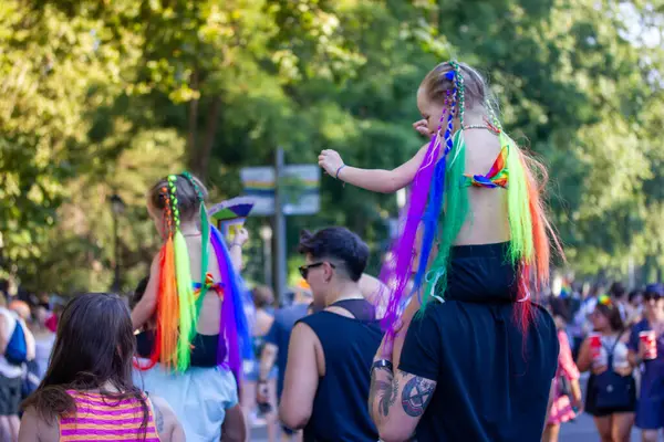 Madrid, İspanya. 1 Temmuz 2022 'de çocuklu insanlar yaz günü gay aylarında geçit töreninde eğleniyorlardı. LGBT gökkuşağı renginde fiyonklu küçük kızlar.