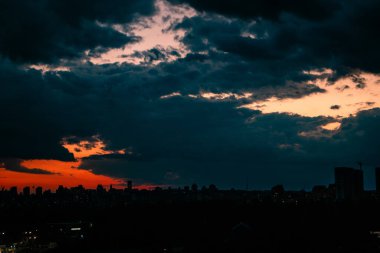 Karanlık akşam mavi-kırmızı gökyüzü ve ufuktaki yüksek binaların silueti. Akşam manzarası. Alacakaranlıkta kızıl gökyüzü. Gece vakti şehir manzarası
