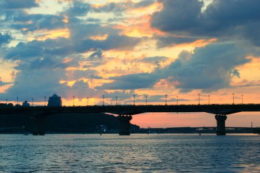 Kyiv, Ukrayna. 1 Mayıs 2021 Sakin nehir boyunca uzanan bir köprü silueti canlı bir günbatımı gökyüzü altında, renkli bulutlar altında, suya yansıyan ışık. 