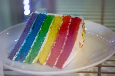 Canlı bir dilim gökkuşağı pastası. Renkli bir tatlı. Kutlamalar ya da tatlı anlar için mükemmel. Pasta beyaz tabakta sunuluyor Neşeli gurur tatlı
