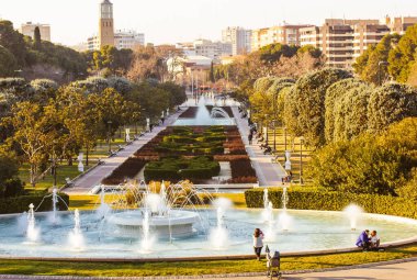 Zaragoza, İspanya 1 Nisan 2022 fıskiyeler, ağaçlar ve bir kuleye ve şehir binalarına giden uzun bir patika olan pitoresk bir park sahnesi. Şehir manzarası