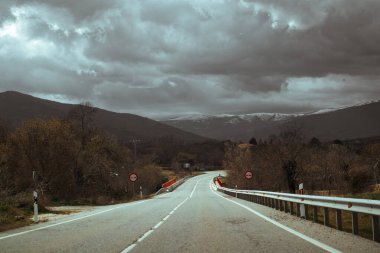 Navacerrada, İspanya 1 Şubat 2024 Bulutlu bir günde bir vadi boyunca uzanan manzaralı bir otoyol, Dağların tepeleri karlı