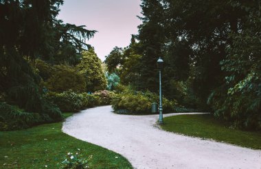 Sarmal bir çakıl yolu, ağaçlar ve manikürlü çimlerle çevrili yemyeşil bir parktan geçerek sakin bir açık hava manzarası yaratır. Huzurlu bir yaz parkı.