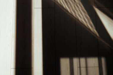 Güneş ışığı, ahşap zeminde geometrik gölgeler yaratarak soyut desenler oluşturur. Ahşap zemin ve pencere ve gölgeleri gösteren soyut resim.