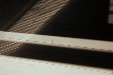 Güneş ışığı, ahşap zeminde geometrik gölgeler yaratarak soyut desenler oluşturur. Ahşap zemin ve pencere ve gölgeleri gösteren soyut resim.