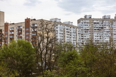 Kyiv, Ukrayna. 1 Nisan 2025. Bulutlu bir günde, ön planda ağaçlar olan apartman binaları dik duruyor. Büyük şehirde şehir mimarisi.