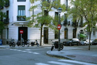 Madrid, İspanya 1 Eylül 2025 Bir şehir manzarası sokak köşesini gündüz yakalıyor, mimari ve çeşitli araçlar sergileniyor. Yeşil şehir sokağı