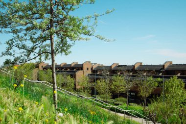 Madrid, İspanya 1 Mayıs 2024 canlı bir sahne, önde bir ağaçla yemyeşil çimlerin ortasındaki modern evleri yakalar. Mavi gökyüzünün altında küçük bir kasaba. 