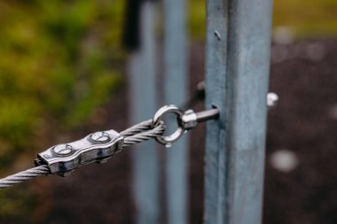 Metal bir kabloyu direğe bağlayıp güçlü bağlantılarını gösteren detaylı bir görüntü. Yağmurda açık havada parlak bir kablo bağlantısının yakın çekimi. 