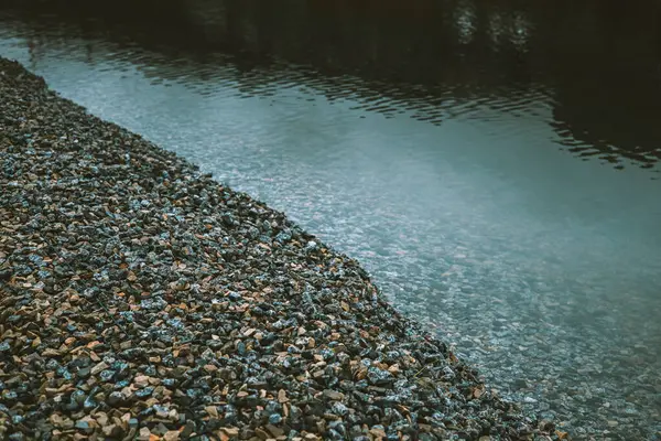 Sakin bir sahne - taşlardan oluşan bir kıyı şeridi bir nehrin sakin sularıyla buluşuyor. Bir su kütlesinin kenarının soyut görünümü, çapraz ayrım çizgisi ile