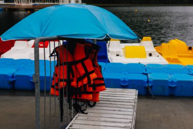 Göl kıyısındaki tatil köyünde renkli pedal tekneleri, güvenlik ekipmanları ve mavi bir şemsiye su eğlencesi sağlıyor. Su maceralarına hazır bir can yelekleri Yaz tatili