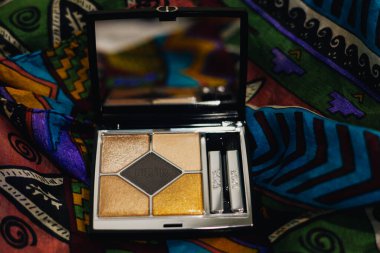 Paris, Fransa. 1 Mayıs 2025 Zarif Dior göz falı paleti, şık bir makyaj aksesuarı, canlı, ipek renkli bir kadın eşarbında sanatsal bir şekilde sergileniyor..