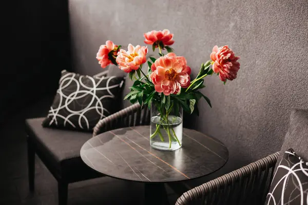 Vazodaki mercan şakayıklarının çarpıcı bir düzeni modern bir masada rahat bir şekilde oturmaktadır. Masada bahar çiçekleri olan bir çiçek aranjmanı..