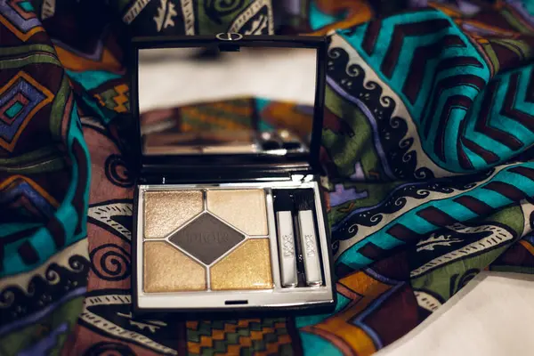 Paris, Fransa. 1 Mayıs 2025 Zarif Dior göz falı paleti, şık bir makyaj aksesuarı, canlı, ipek renkli bir kadın eşarbında sanatsal bir şekilde sergileniyor..