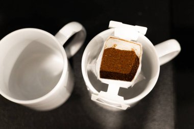 İki beyaz kahve fincanı, birinin kahve poşeti taze ve lezzetli bir fincan demlemeye hazır. Bardaklar aromatik kahve için hazır, eğlenmeye hazır..