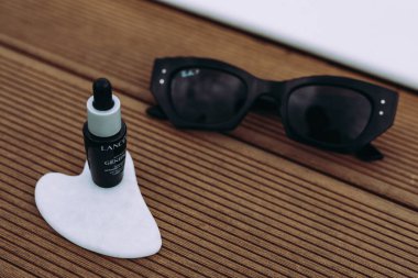 Bukovel, Ukrayna 7 Mayıs 2025 güneş gözlüğü, cilt bakımı aleti, ahşap zemin üzerinde serum şişesi. Yüz masajı aletleri. Cilt bakımı, rahatlama