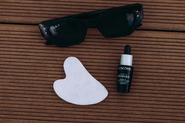 Bukovel, Ukrayna 7 Mayıs 2025 güneş gözlüğü, cilt bakımı aleti, ahşap zemin üzerinde serum şişesi. Yüz masajı aletleri. Cilt bakımı, rahatlama