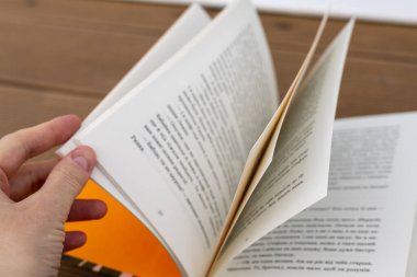 Bukovel, Ukrayna 14 Mayıs 2025 Bir el açık bir kitabın sayfalarını çevirir, basılmış kelimeleri ve taze kağıdı keşfeder. Tahta bir yüzey üzerine bir kitap..