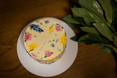 Taze yeşil yapraklarla yakalanmış, narin elle boyanmış çiçeklerle dolu bir doğum günü pastası. Elle boyanmış çiçeklerle süslenmiş güzel dekore edilmiş bir pasta. Kutlamalar için mükemmel. Yukarıdan görüntüle.