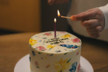 Bir el pastanın üzerine mum yakıyor. Çiçeklerle süslenmiş, eğlenmeye hazır. Bir el, güzel bir doğum günü pastasının üzerine mum yakar. Bir şenlikli pasta çiçeklerle süslenir.. 