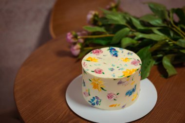 Güzel dekore edilmiş bir çiçek pastası taze şakayıkların yanındaki ahşap bir masada oturur. Kutlamalar için mükemmel, şakayıklı ahşap bir masaya yerleştirilmiş.. 