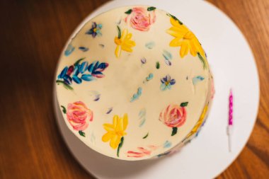 Doğum günü kutlaması için tek bir mumla el boyaması bir çiçek pastası. Çok güzel dekore edilmiş bir pastanın, el boyaması çiçek desenleri ve pembe bir mumla tepe üstü çekilmiş resmi..