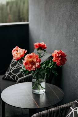 Vazodaki mercan şakayıklarının çarpıcı bir düzeni modern bir masada rahat bir şekilde oturmaktadır. Masada bahar çiçekleri olan bir çiçek aranjmanı..