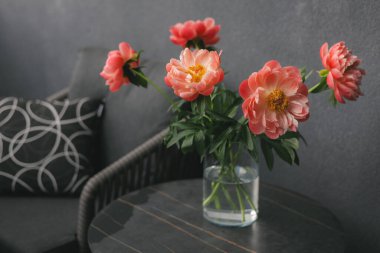 Vazodaki mercan şakayıklarının çarpıcı bir düzeni modern bir masada rahat bir şekilde oturmaktadır. Masada bahar çiçekleri olan bir çiçek aranjmanı..