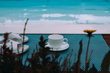 Sakin bir sahnede yazın havuz kenarında bir fincan, terlik ve çiçek sergilenir. Sakin bir havuz kenarında içki içilir. Sakin mavi su. Yaz havası. 