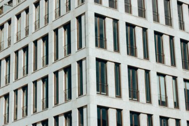 Bir binanın ön cephesinin modern kentsel mimari görüntüsü, birbirinin tıpatıp aynısı çok sayıda dikdörtgen pencere ve balkon içeriyor ve minimalist bir tasarım sergiliyor..