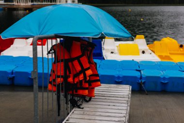 Göl kıyısındaki tatil köyünde renkli pedal tekneleri, güvenlik ekipmanları ve mavi bir şemsiye su eğlencesi sağlıyor. Su maceralarına hazır bir can yelekleri Yaz tatili