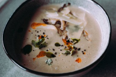 Peynir ve otlarla kaplı bir kasede servis edilen lezzetli kremalı mantar çorbası. Parmesan peyniri ve mikroyeşillikle süslenmiş, yemeye hazır bir çorba..