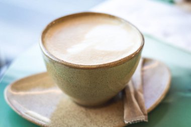 Lezzetli bir bardak kapuçino, güne başlamak için mükemmel bir yol. Sıcak, davetkar bir fincan kapuçino, yanında bir şeker paketi bulunan bir fincan tabağın üzerinde, tadını çıkarmaya hazır. Düz latte sanatı içkinin üstünde..