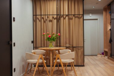 Modern bir yemek salonunda bir dairede yuvarlak masa, sandalyeler ve zarif bej perdeler bulunur. Konforlu iç mekan küçük bir yemek alanı gösteriyor..