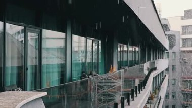 Dışarıdan düşen kar taneleri kasvetli bir kış gününde şehir manzarasına bakan modern bir balkon. Bir balkon manzarası, modern şehir mimarisi..