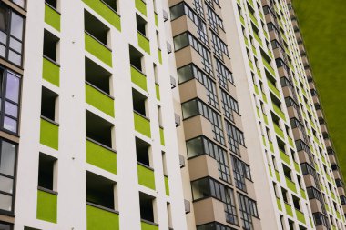 Modern beyaz bir tasarımı olan uzun bir apartmanın düşük açılı çekimi, yeşil aksanlı eşsiz bir renk şeması gösteriyor. Mahalle sakinleri. 
