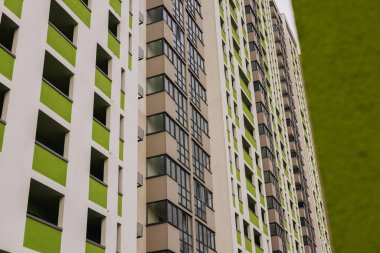 Modern beyaz bir tasarımı olan uzun bir apartmanın düşük açılı çekimi, yeşil aksanlı eşsiz bir renk şeması gösteriyor. Mahalle sakinleri. 