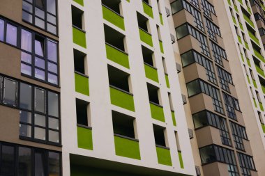 Modern beyaz bir tasarımı olan uzun bir apartmanın düşük açılı çekimi, yeşil aksanlı eşsiz bir renk şeması gösteriyor. Mahalle sakinleri. 