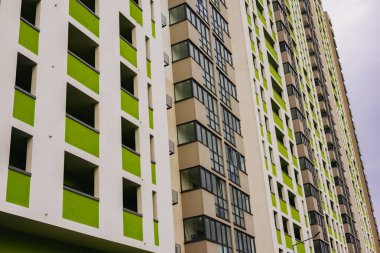 Modern beyaz bir tasarımı olan uzun bir apartmanın düşük açılı çekimi, yeşil aksanlı eşsiz bir renk şeması gösteriyor. Mahalle sakinleri. 