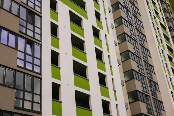Modern beyaz bir tasarımı olan uzun bir apartmanın düşük açılı çekimi, yeşil aksanlı eşsiz bir renk şeması gösteriyor. Mahalle sakinleri. 