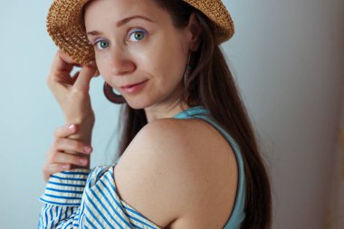 Hasır şapkalı bir kadın gülümsüyor, yumuşak ışıklandırmalı davetkar bir portre oluşturuyor. Şapka, kolye ve halka küpeler takan bir kadın gülümseyerek doğal ışıkta sıcak, davetkar bir portre çizer..