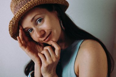 Hasır şapkalı bir kadın gülümsüyor, yumuşak ışıklandırmalı davetkar bir portre oluşturuyor. Şapka, kolye ve halka küpeler takan bir kadın gülümseyerek doğal ışıkta sıcak, davetkar bir portre çizer..