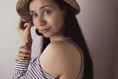 Hasır şapkalı bir kadın gülümsüyor, yumuşak ışıklandırmalı davetkar bir portre oluşturuyor. Şapka, kolye ve halka küpeler takan bir kadın gülümseyerek doğal ışıkta sıcak, davetkar bir portre çizer..