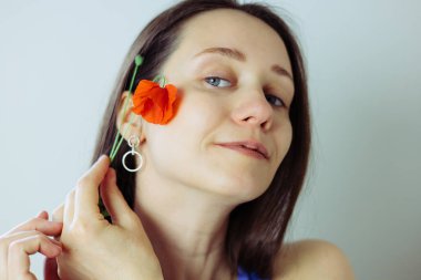 Çekici beyaz kadın elinde canlı kırmızı bir gelincik çiçeğiyle zarif poz veriyor, yakın plan. Kendine güvenen bir kız şık, minimumda küpeler takıyor..