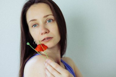 Güzel, esmer, genç, beyaz bir kadın, koyu saçlı kırmızı bir gelincik ile izleyiciye bakıyor. Yazın doğal kadın güzelliği. 