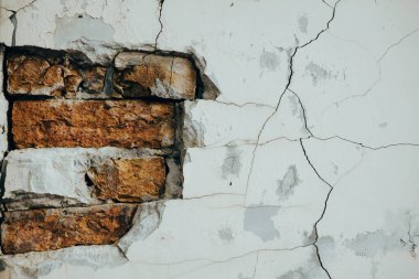Çürüme ve yaşlanma belirtileri gösteren çatlak boyalı eski bir tuğla duvarın detaylı görüntüsü. Yıpranmış tuğla bir duvara yakın çekim yapmak, yapı malzemesinin eskimiş dokusunu ortaya çıkarır..